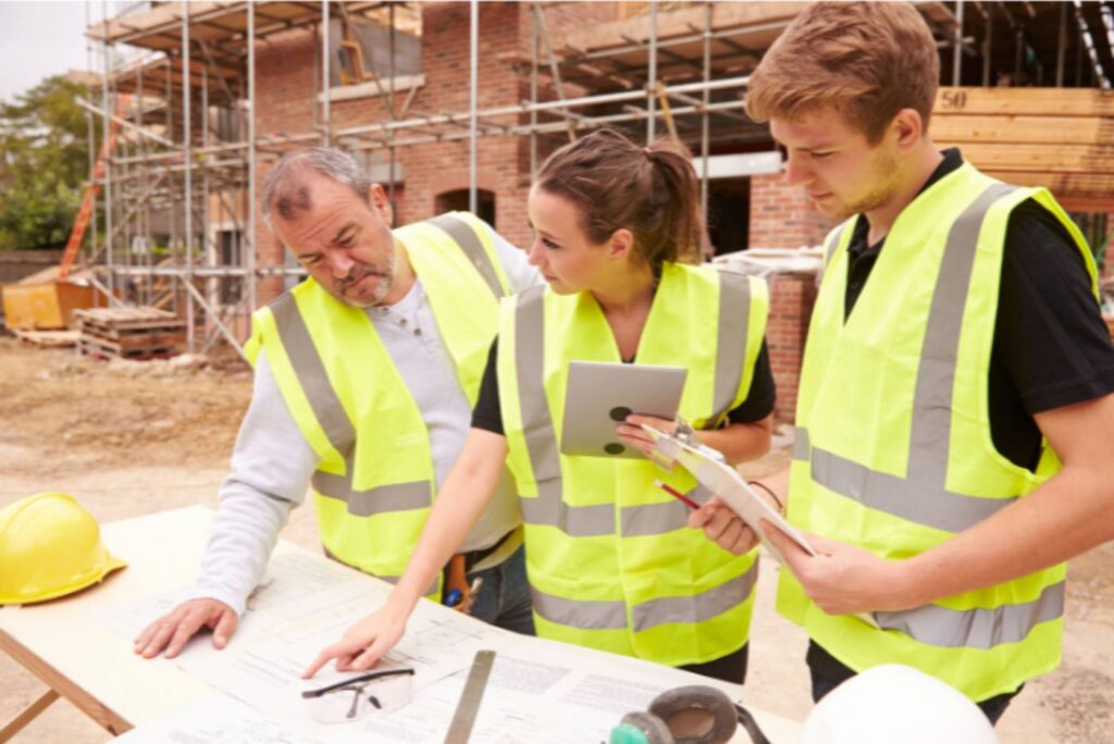Three workers on construction site discussing a blueprint